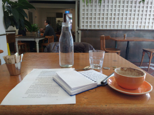 coffee cup, water, writing pad, pen on wooden table in cafe